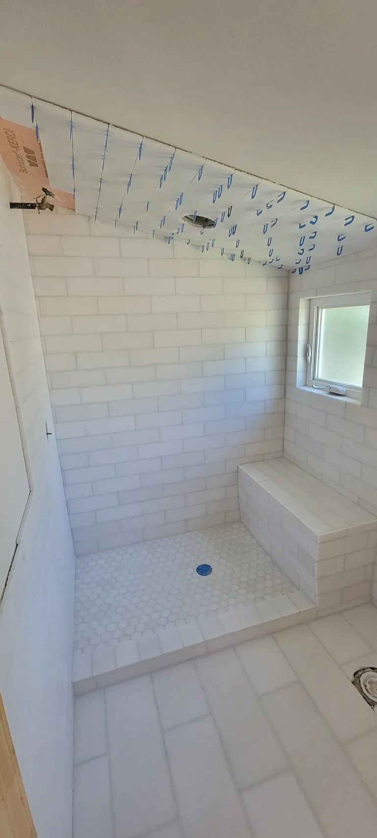 The shower part-tiled, with the orange waterproofing membrane still showing at the ceiling.